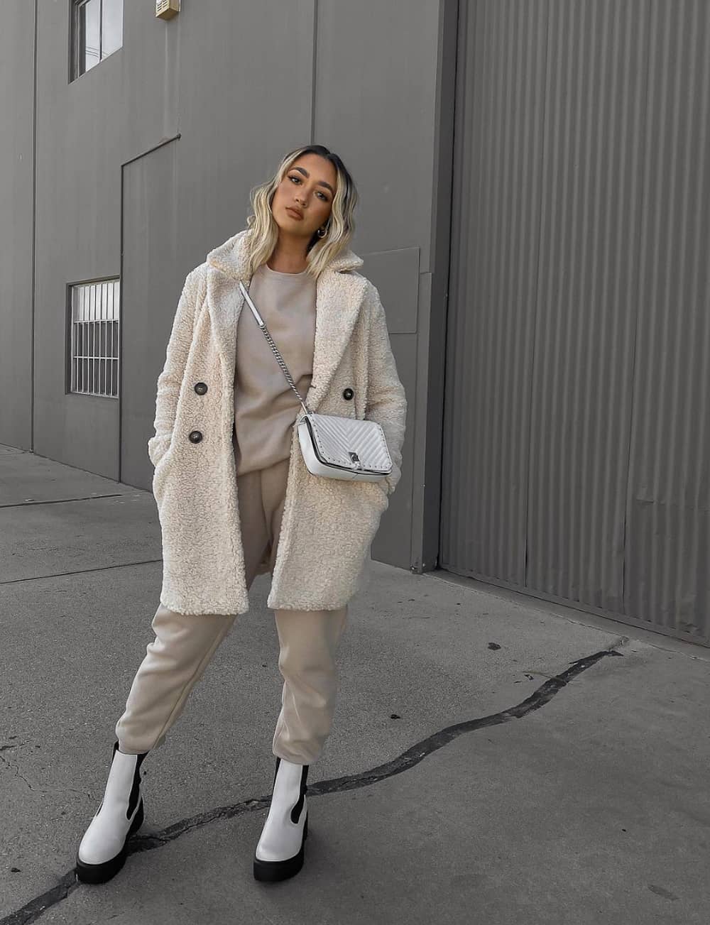 image of a woman wearing a long white shearling coat over a matching taupe sweatsuit with white lug boots