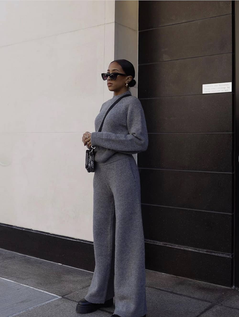 image of a stylish black woman in a matching knit pant set with chunky boots and a designer bag