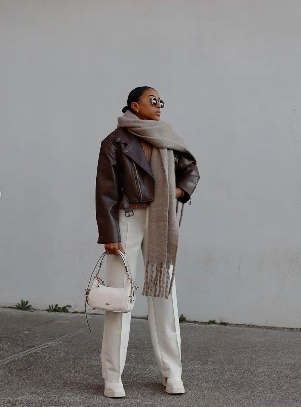 image of a black woman in a cropped brown leather jacket, oversized scarf, and long ivory wool trousers with chunky white boots