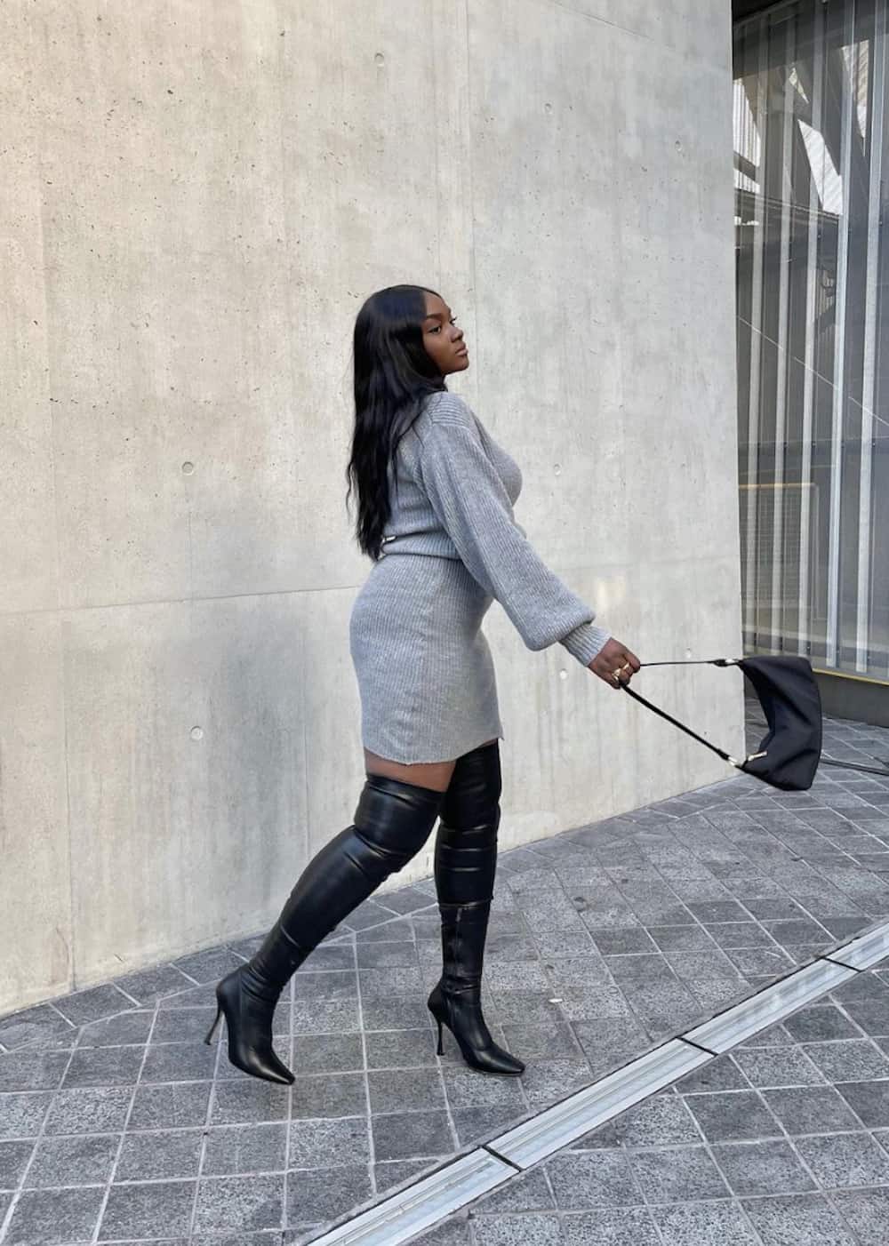 image of a black woman wearing a grey sweater dress, over-the-knee leather boots, and a black bag