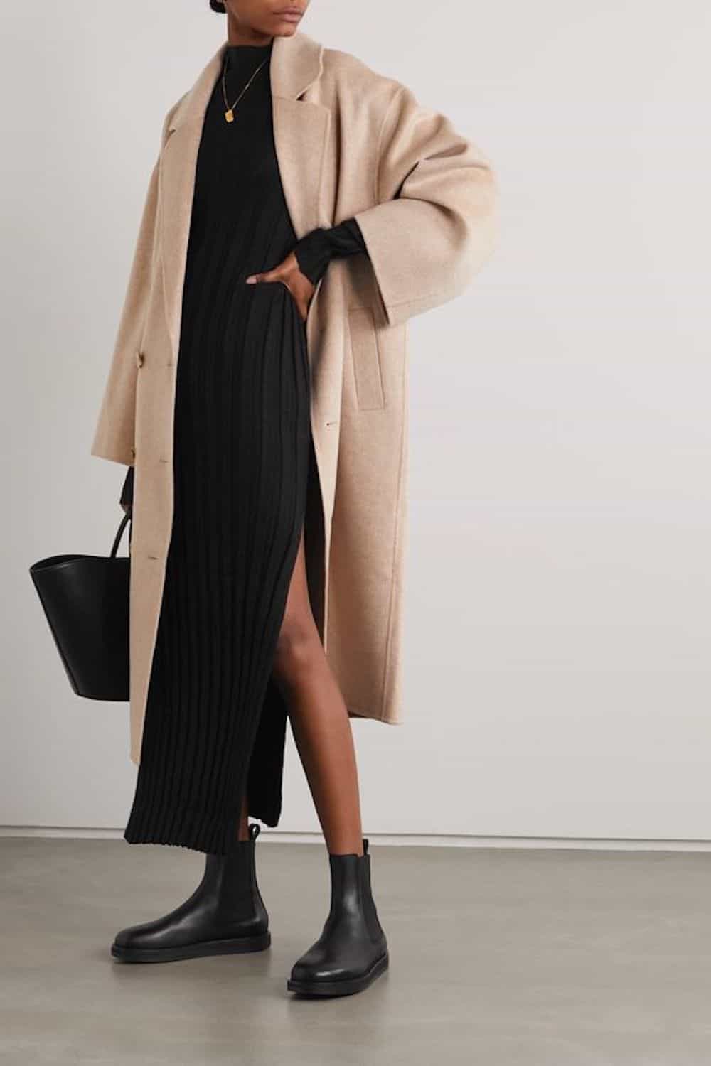 image of a woman from the shoulders down in a long black sweater dress with a wool coat and black lug boots