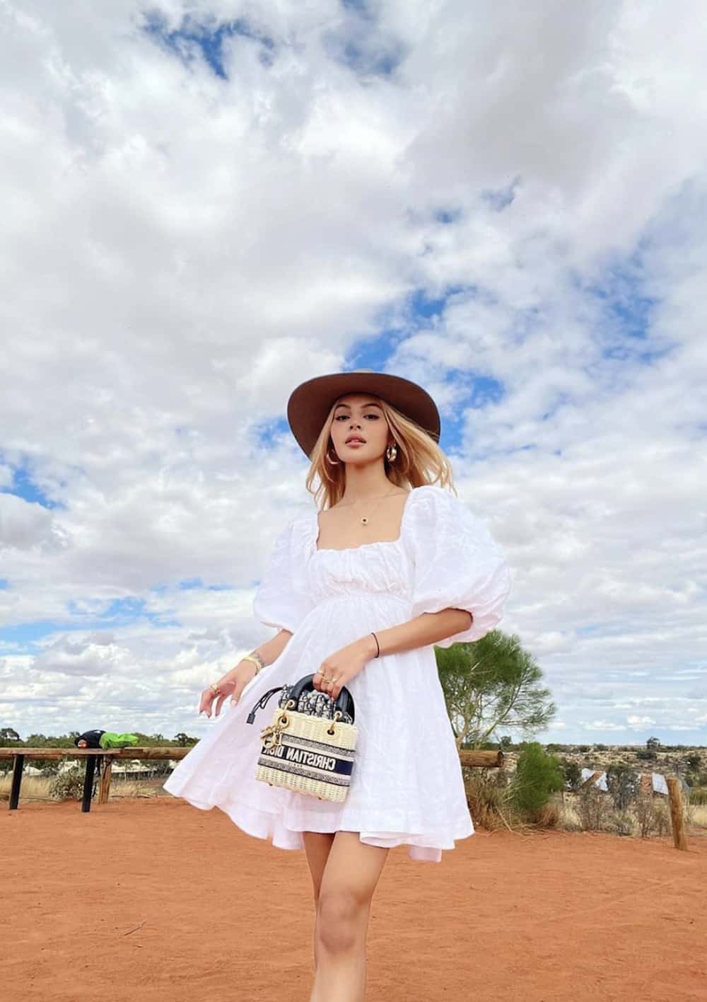 Woman wearing a white mini dress and a brown hat with a Dior bag.