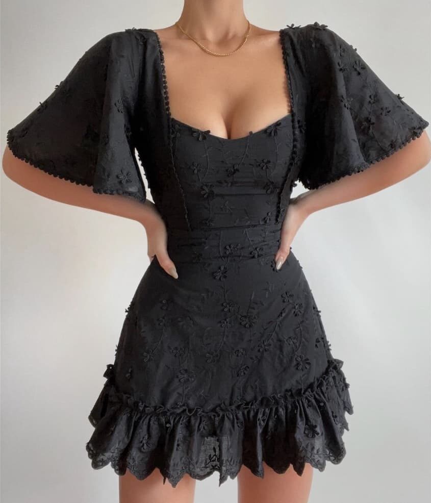 Woman wearing a black lace mini dress with a scalloped hem.