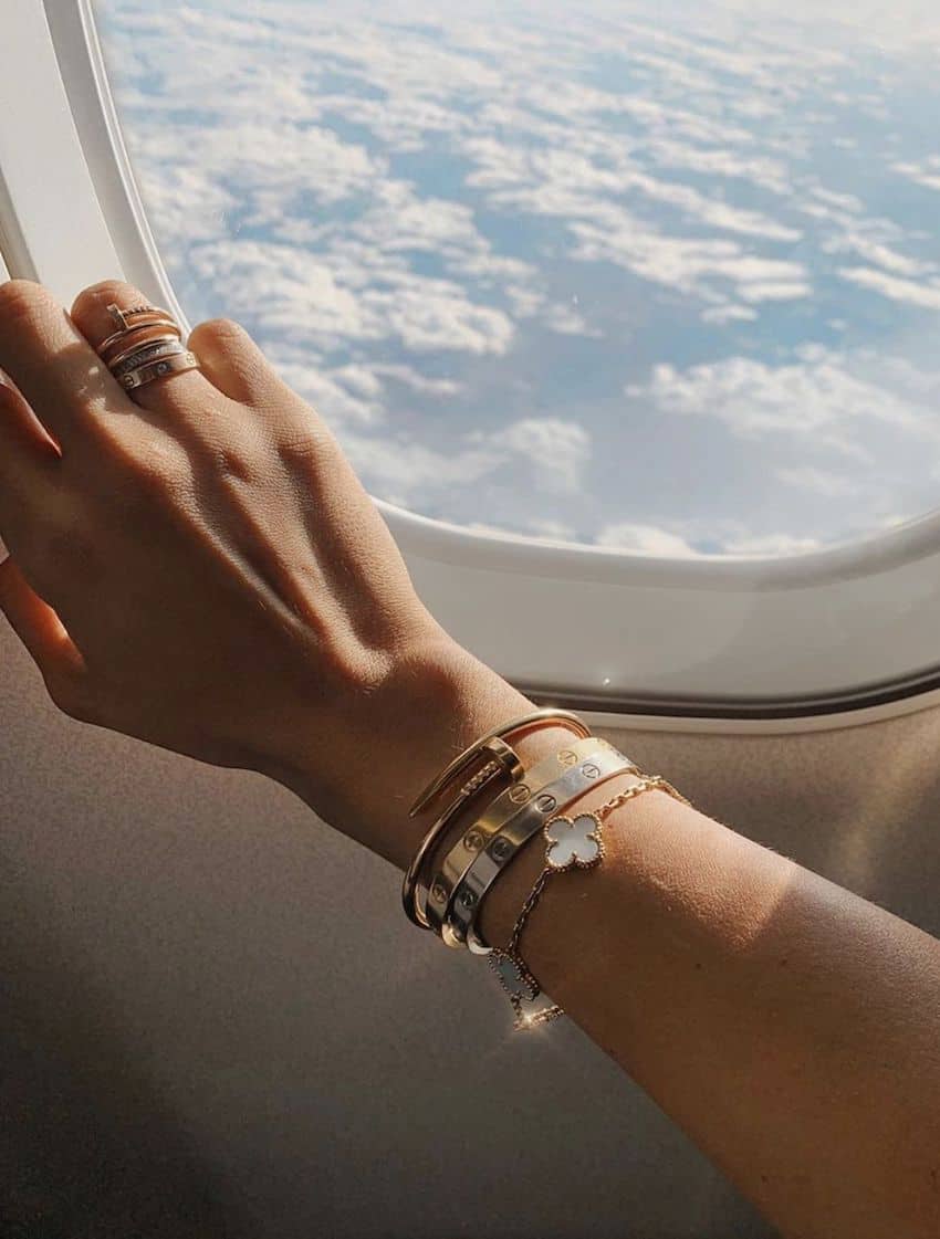 image of a woman's arm in front of an airplane window adorned with a Cartier love bracelet and other fine jewelry