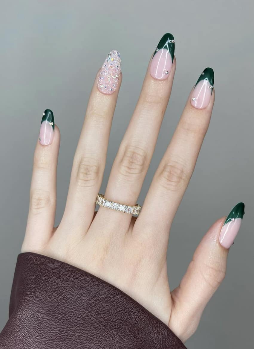 Long rounded nails with an emerald green french tip and accent nail with gemstones.