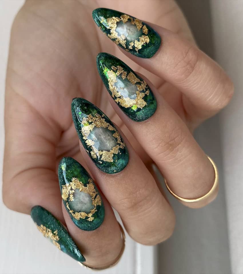 Pointed emerald green nails with gold leafing in a circle.