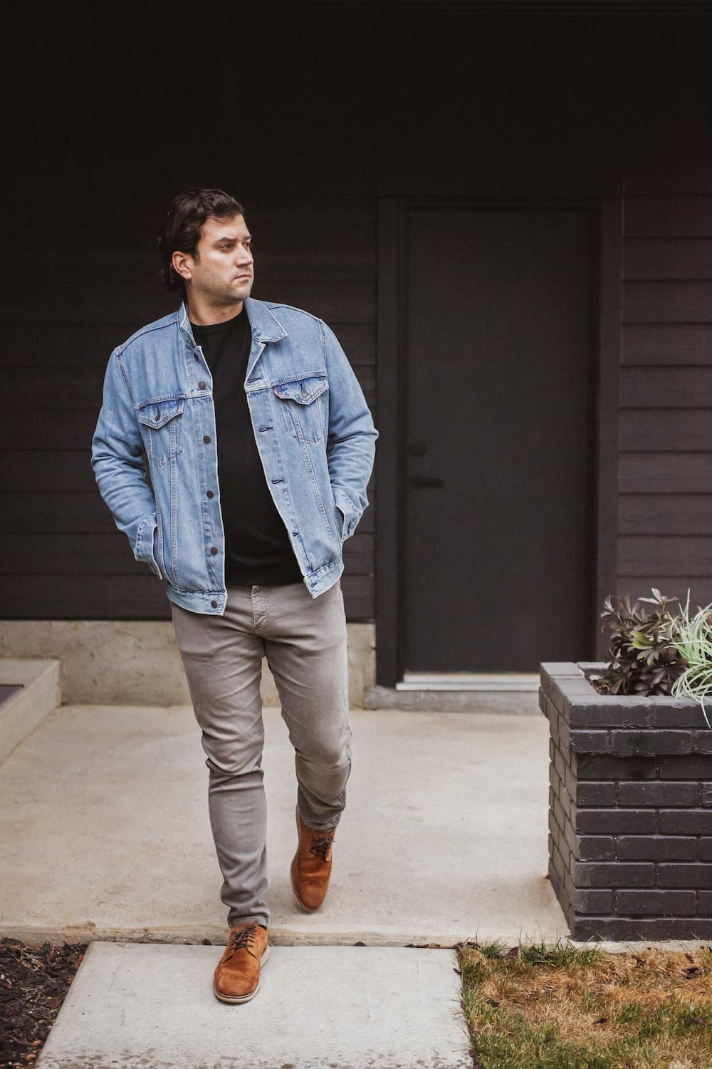 image of a man wearing a denim jacket, black t-shirt, grey chino pants, and brown casual shoes