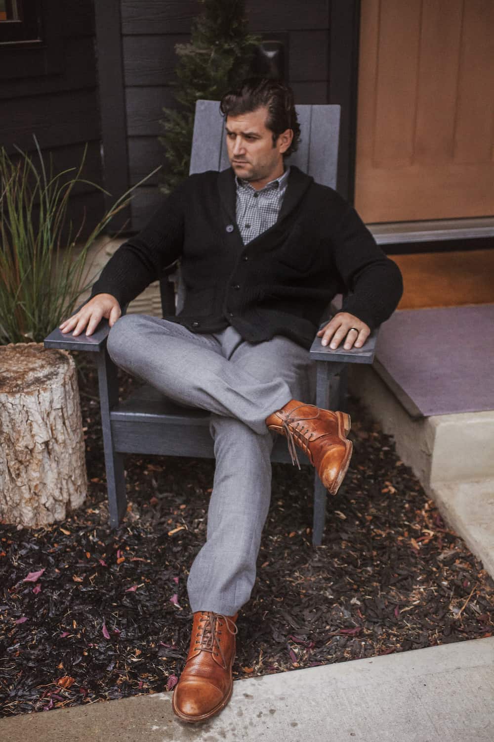 image of a man sitting in a chair wearing light grey pants, brown boots, and a black sweater