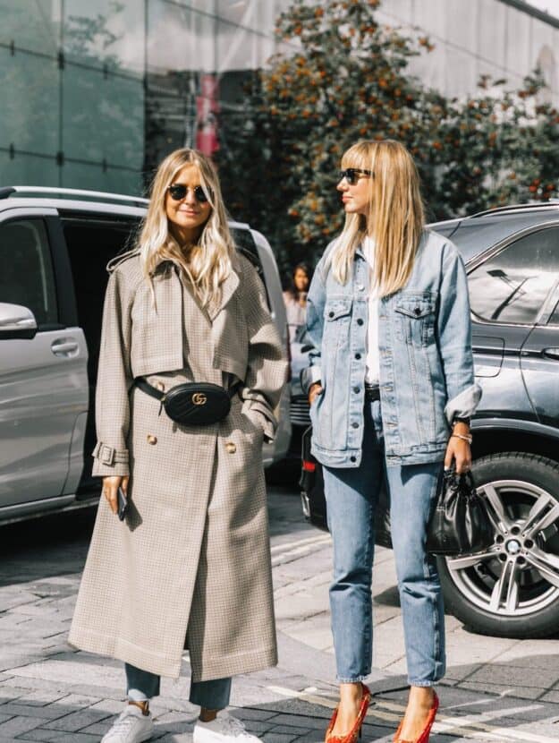 image of two women standing in the street, one wearing a long plaid trench coat with black Gucci waist bag, and the other in a denim jacket and jeans