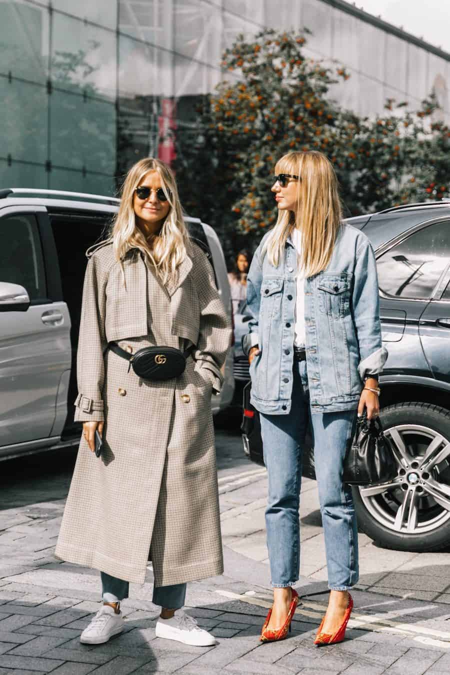 image of two women standing in the street, one wearing a long plaid trench coat with black Gucci waist bag, and the other in a denim jacket and jeans