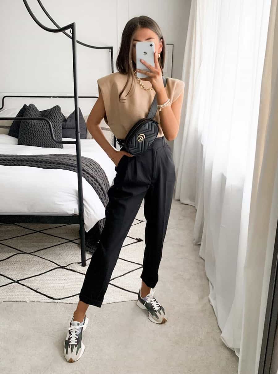 image of a women wearing a tan tank top, black trousers, a black Gucci belt bag, and New Balance sneakers
