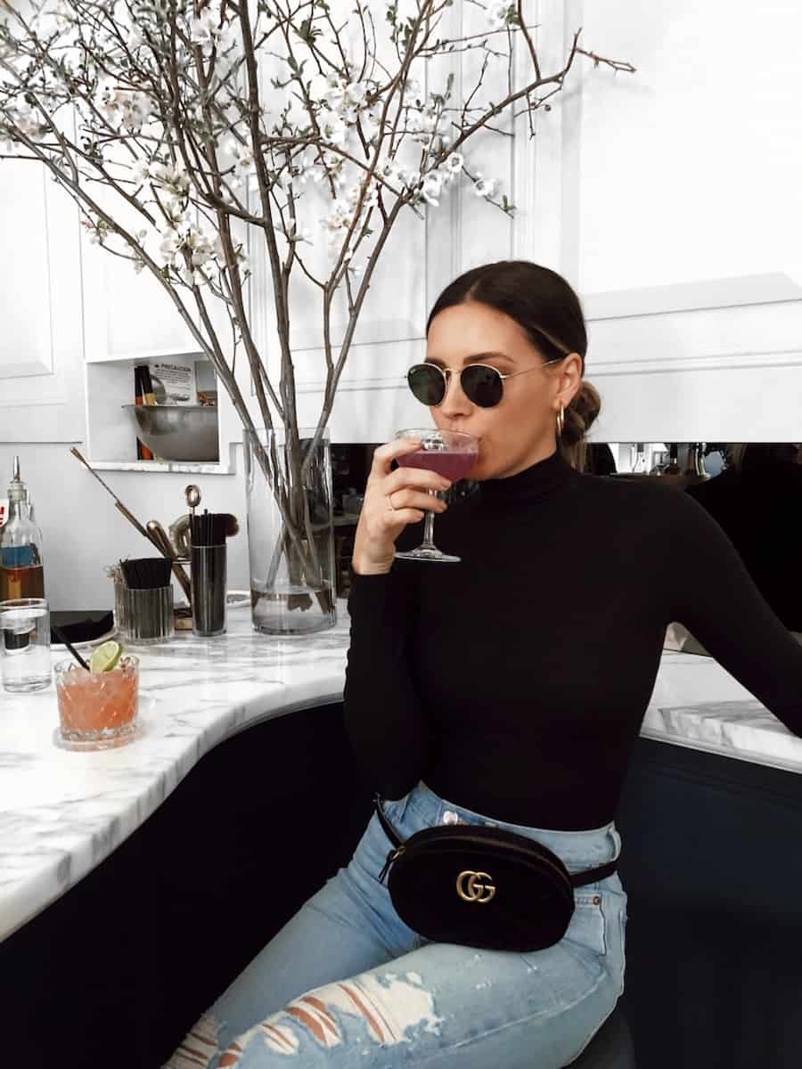 image of a woman wearing a black turtleneck top, blue jeans, and a black suede Gucci Marmont belt bag