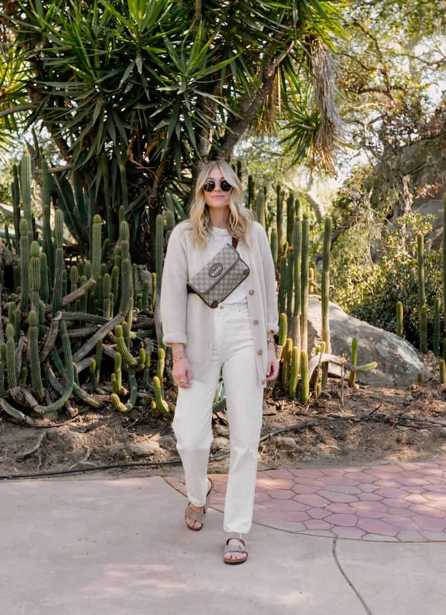 image of a woman wearing an oatmeal oversized cardigan, Gucci supreme sling bag, off white jeans, and suede sandals