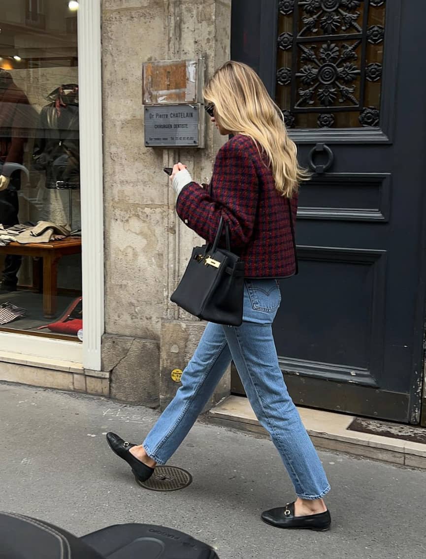 image of a woman walking down the street wearing a cropped maroon tweed jacket, blue jeans, and designer black shoes