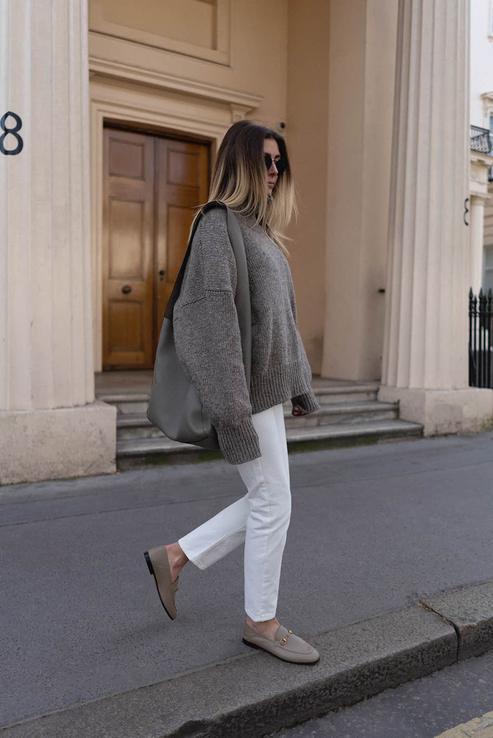 image of a woman in a taupe oversized knit sweater, white jeans and taupe leather loafers