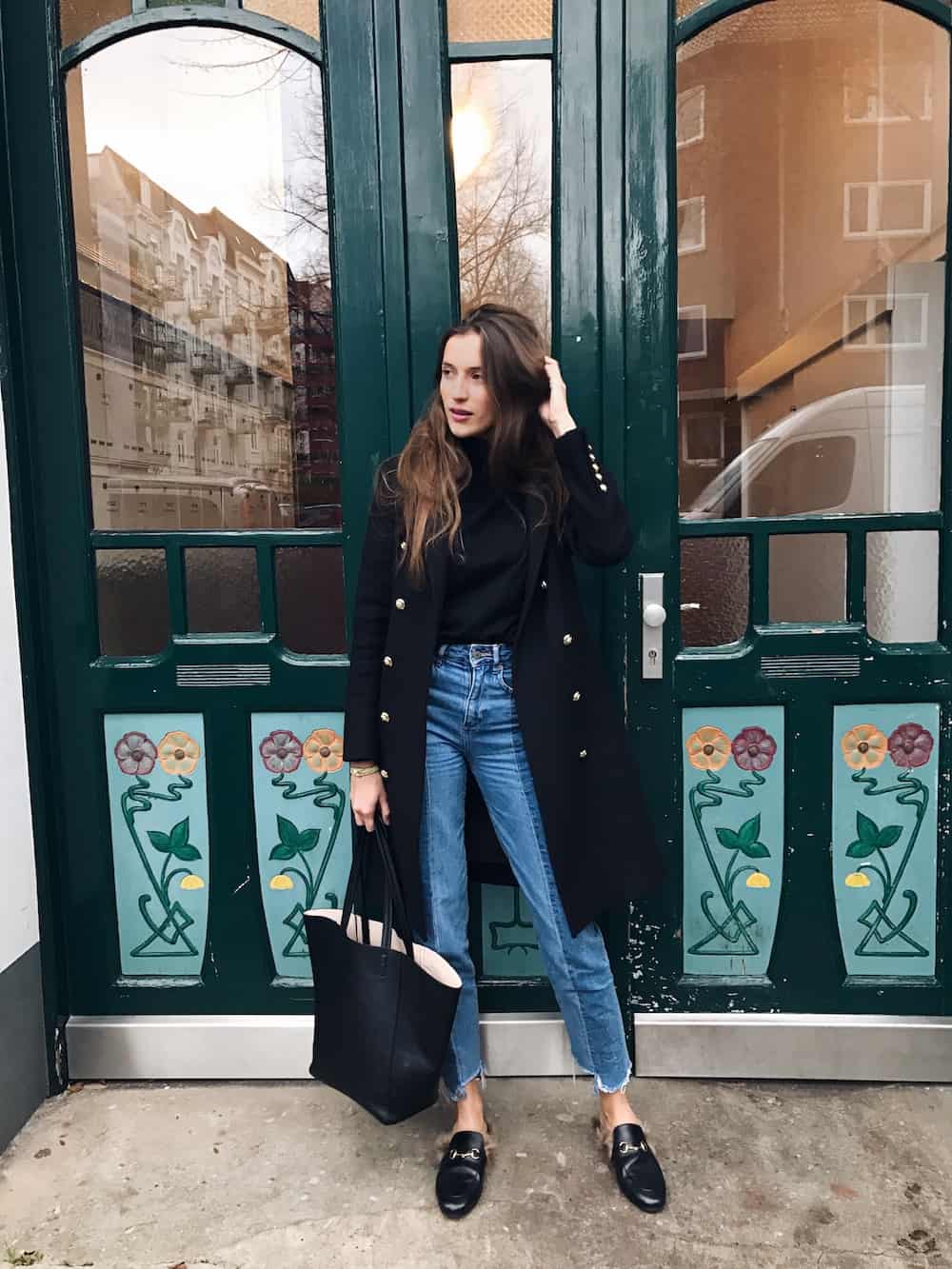 image of a woman wearing a long black wool jacket with distressed blue jeans and black leather mules with fur lining