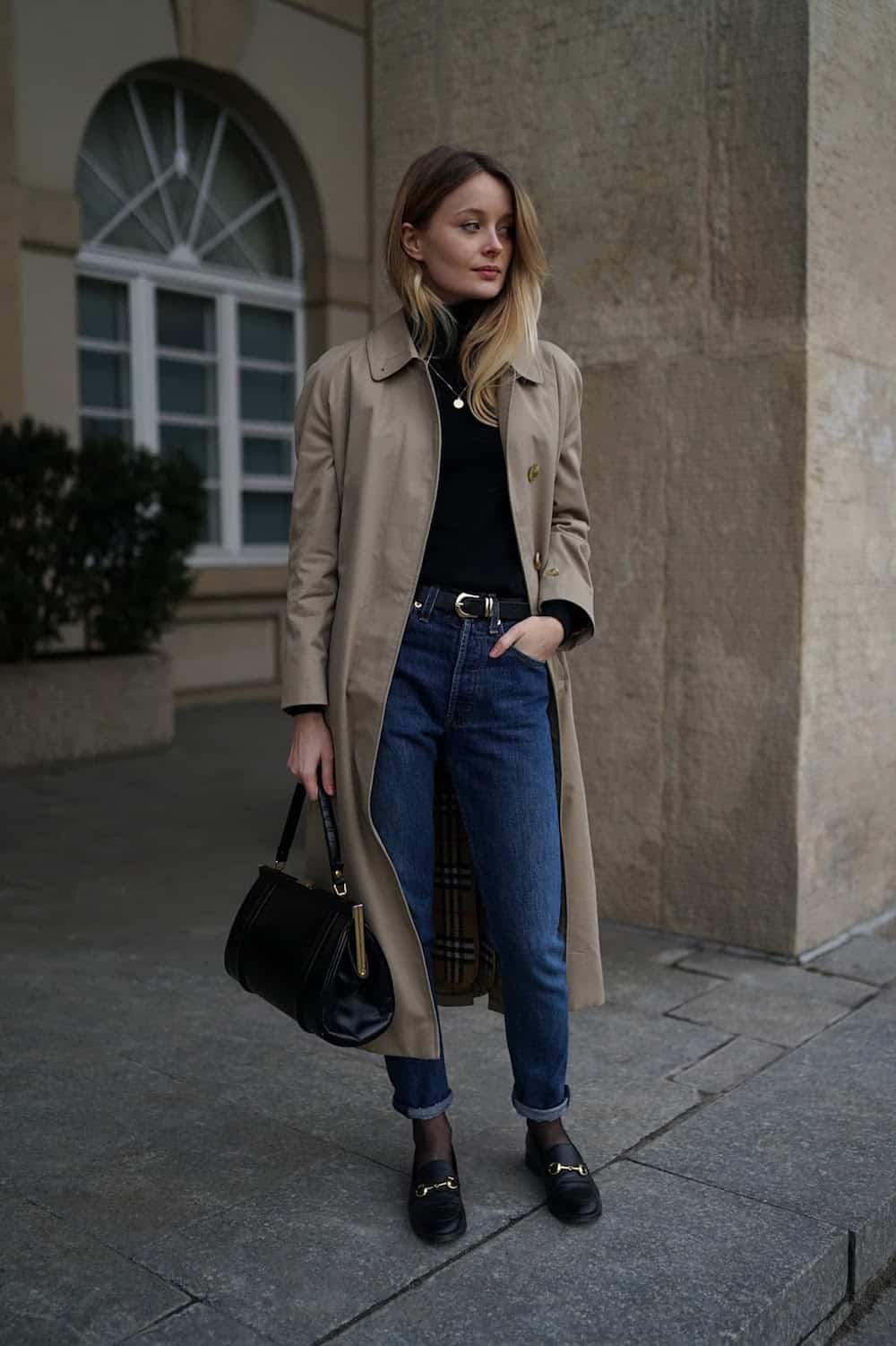 image of a woman in a long trench jacket, black sweater ,blue jeans, and black shoes