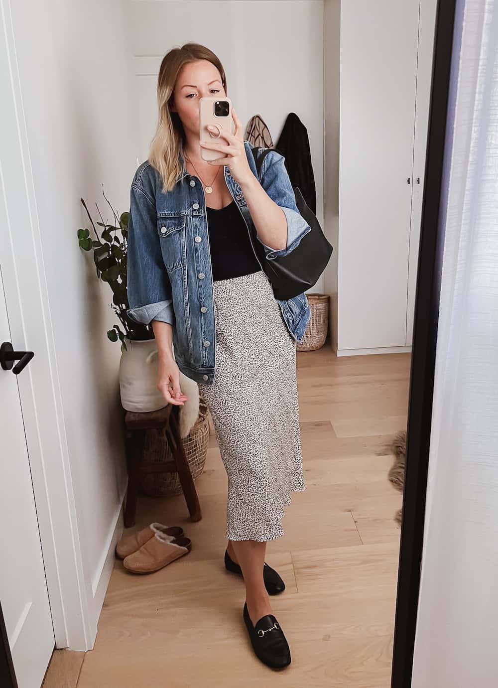 image of a woman wearing an oversized denim jacket, black tank top, midi skirt and black Gucci loafers