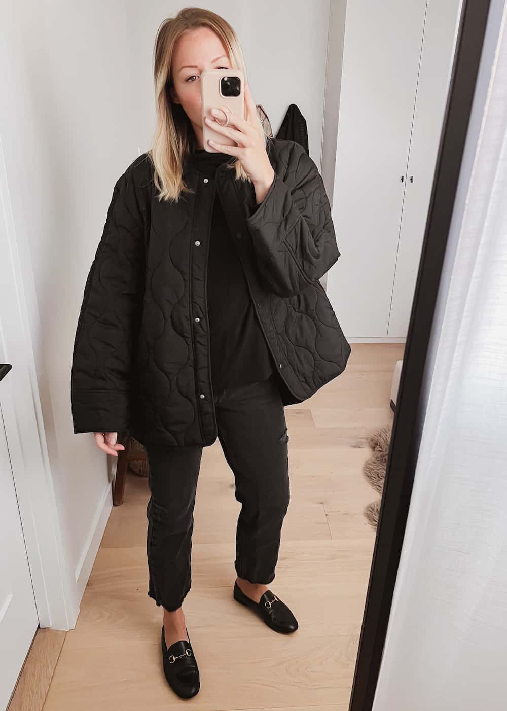 image of a woman in a black quilted jacket, black jeans, and black loafers