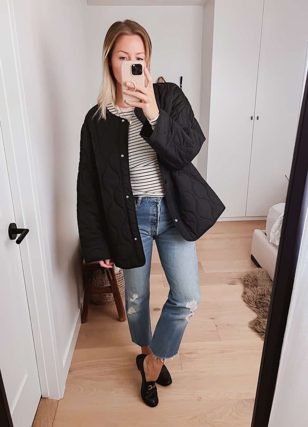 image of a woman in an oversized black quilted jacket over a striped top with blue jeans and black Gucci loafers