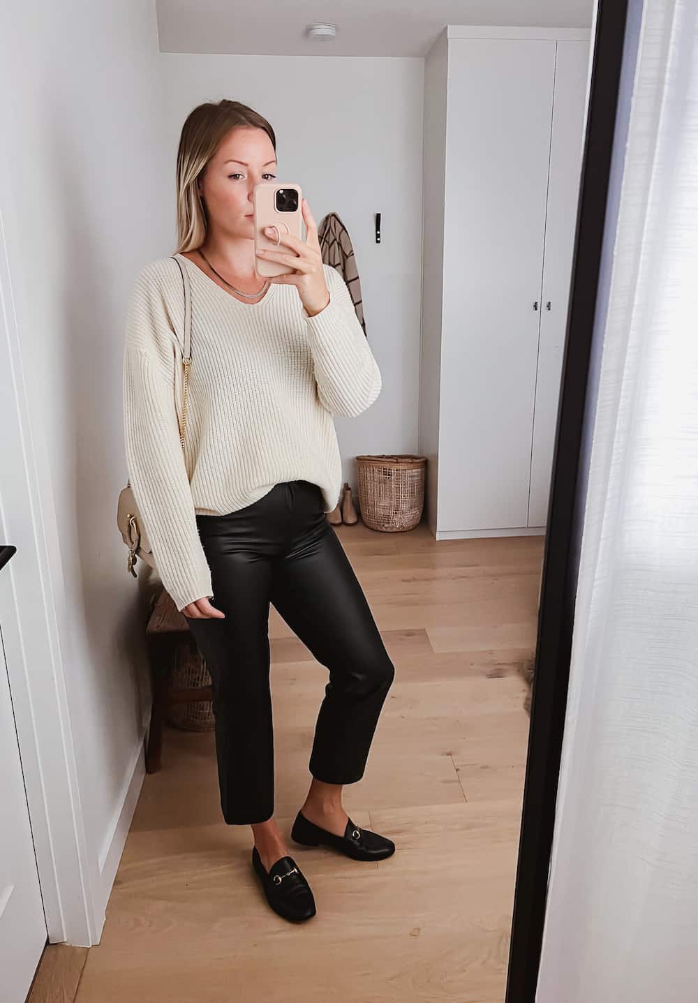 image of a woman wearing an oversized knit ivory sweater and cropped black leather pants with loafers