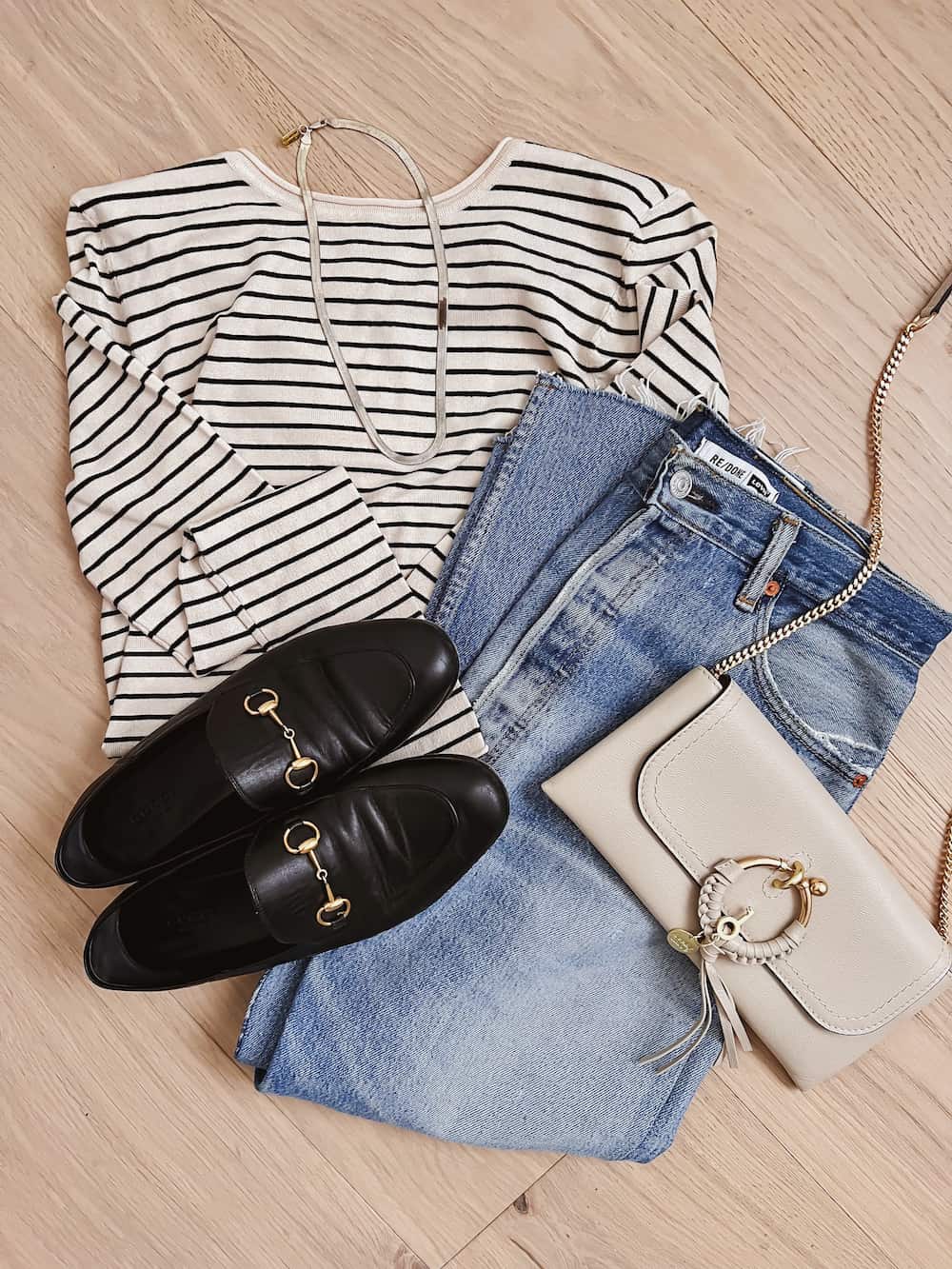 image of an outfit flat lay with blue jeans, black shoes, a striped top and a cream purse