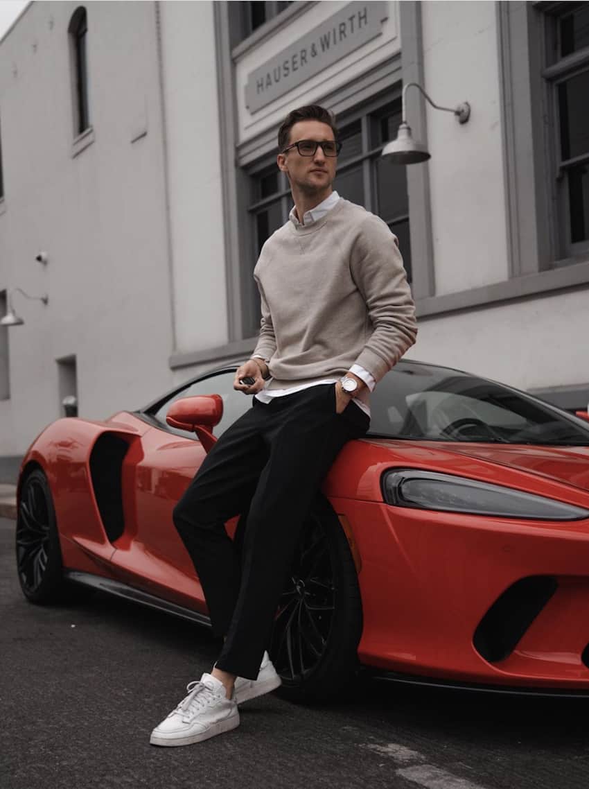 image of a man leaning against a red car wearing dark chino pants and white sneakers with a sweater