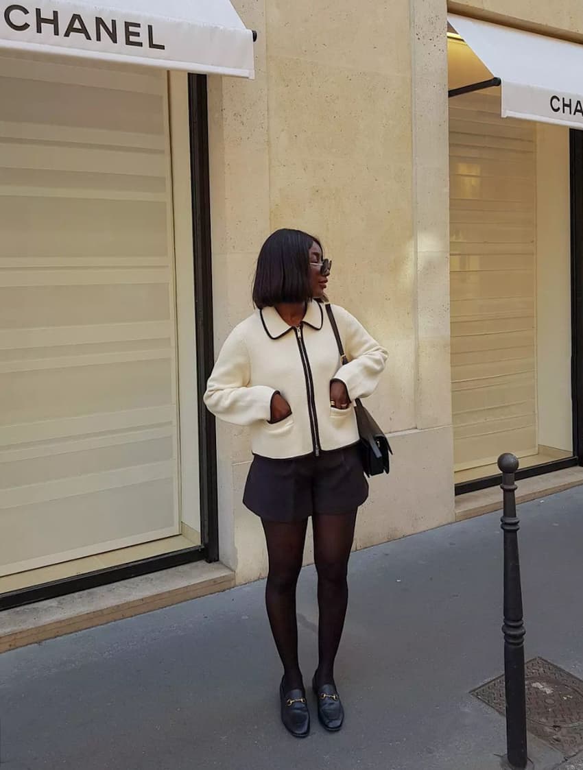 image of a black woman in a cropped ivory jacket, black shorts, tights, and loafers