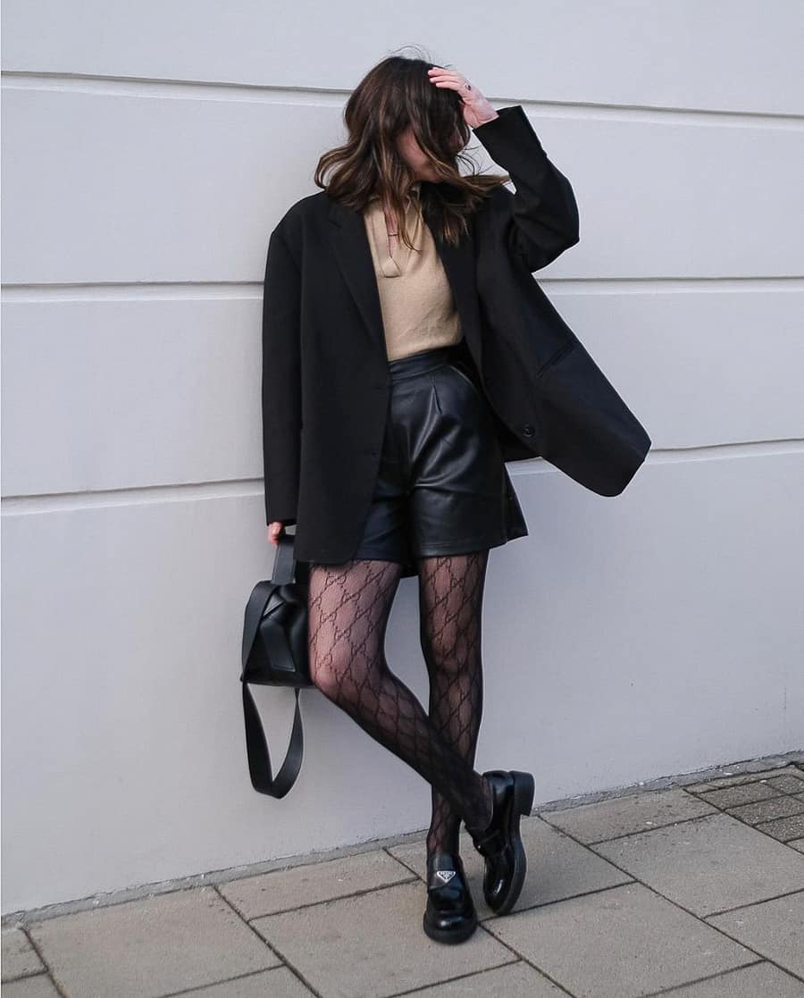 image of a woman in a wool coat, turtleneck sweater, black leather shorts, and printed tights with chunky loafers