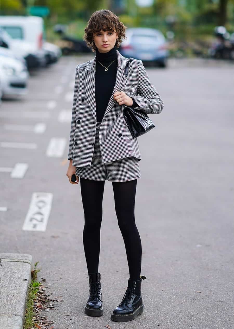 image of a woman wearing a houndstooth blazer and shorts set with black tights and a black turtleneck 