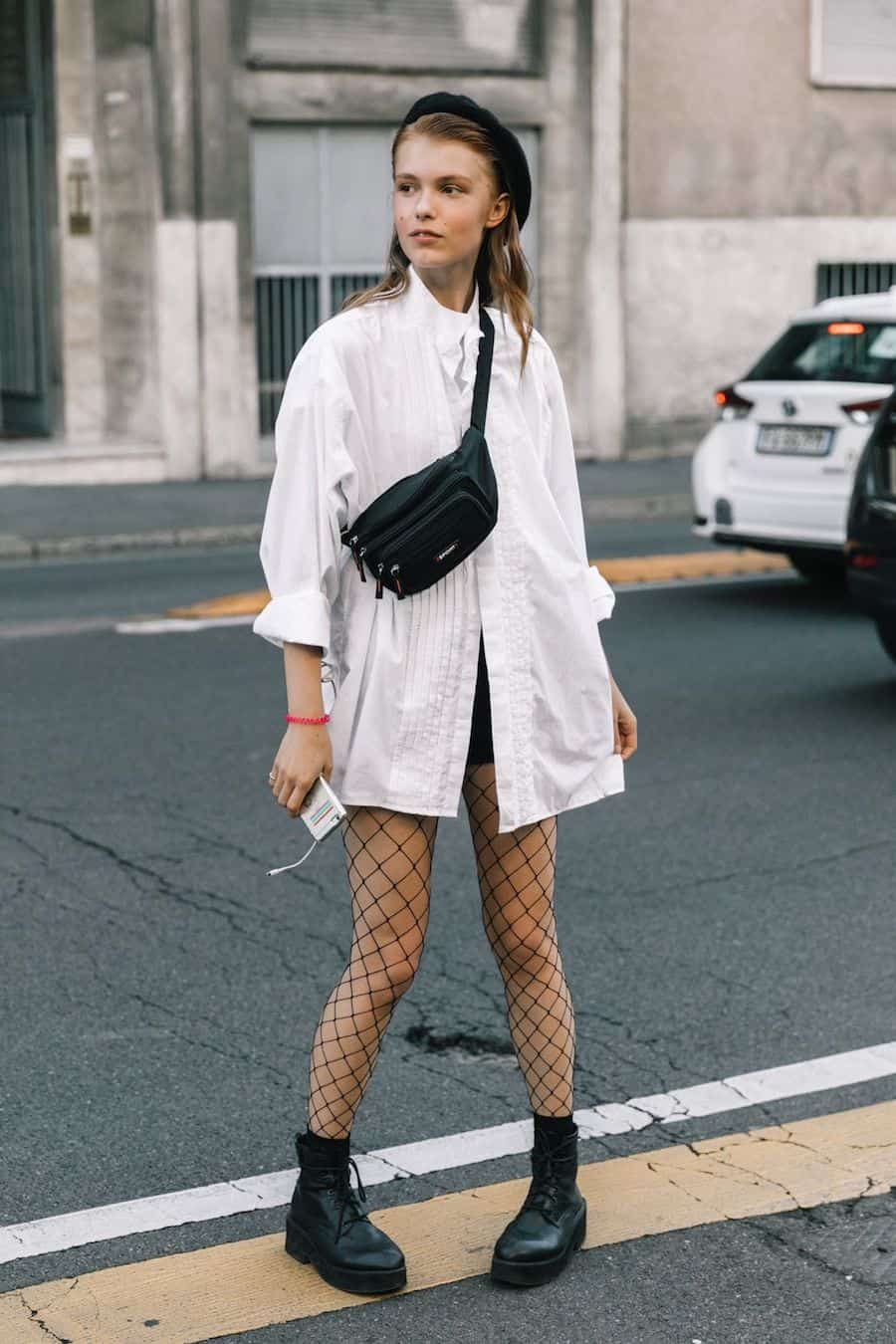 image of a woman wearing a long oversized white button up shirt, shorts, and fishnet stockings