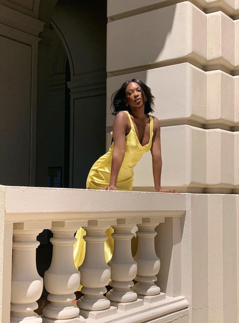 image of a black woman leaning over a balcony wearing a long silk yellow dress