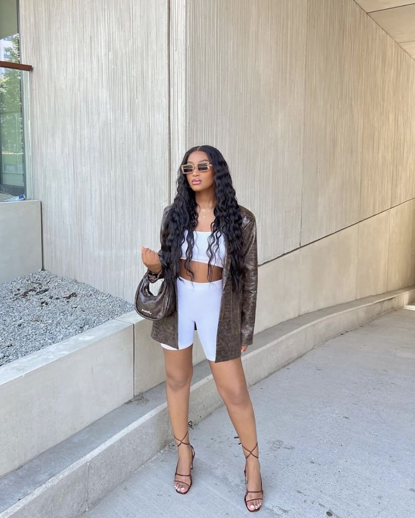 image of a woman in a white biker short and crop top set with a leather blazer and strappy sandals