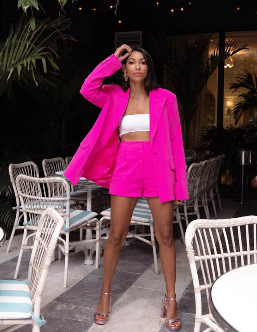 image of a black woman in a neon pink blazer and shorts set with a white tub top and shimmery heels