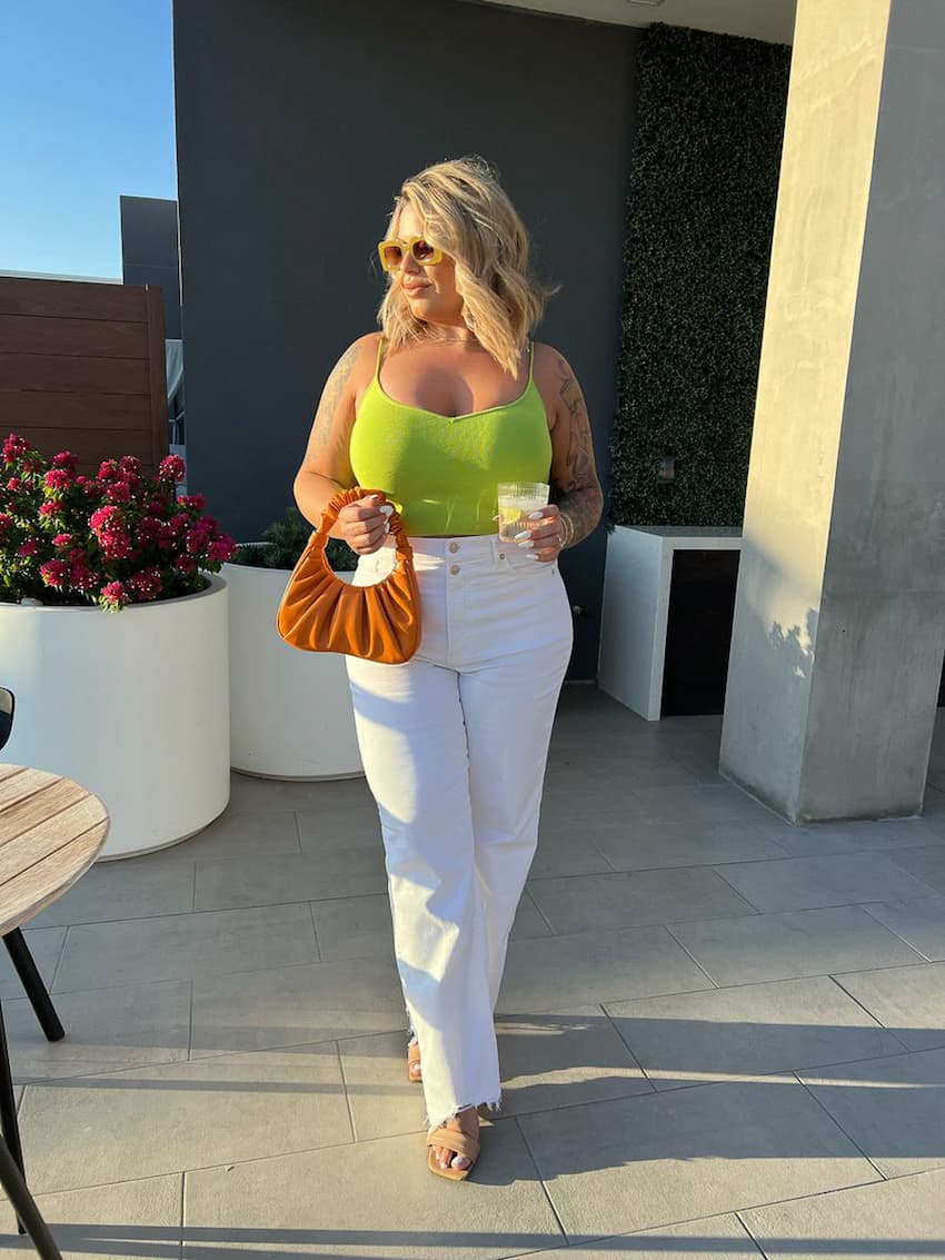 image of a plus size woman wearing a green tank top and white wide leg jeans with heels in Vegas