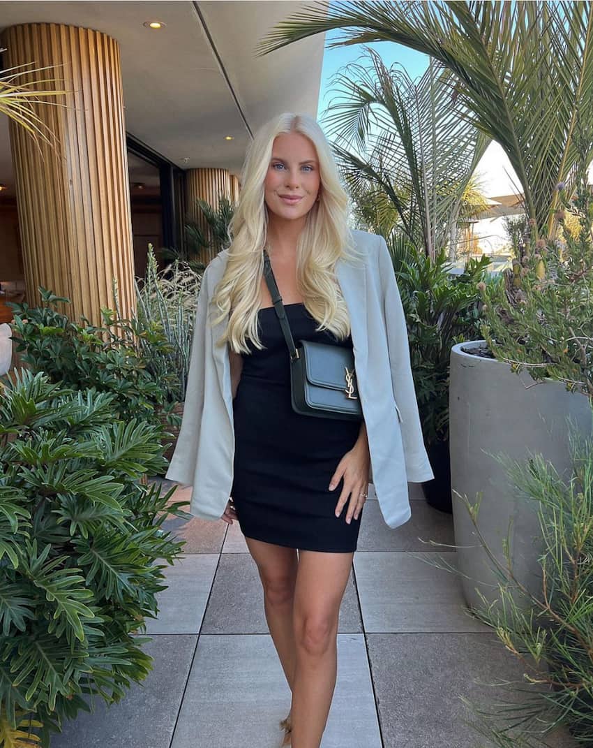 image of a woman with long blonde hair wearing a little black dress, oversized beige blazer, and a designer crossbody bag