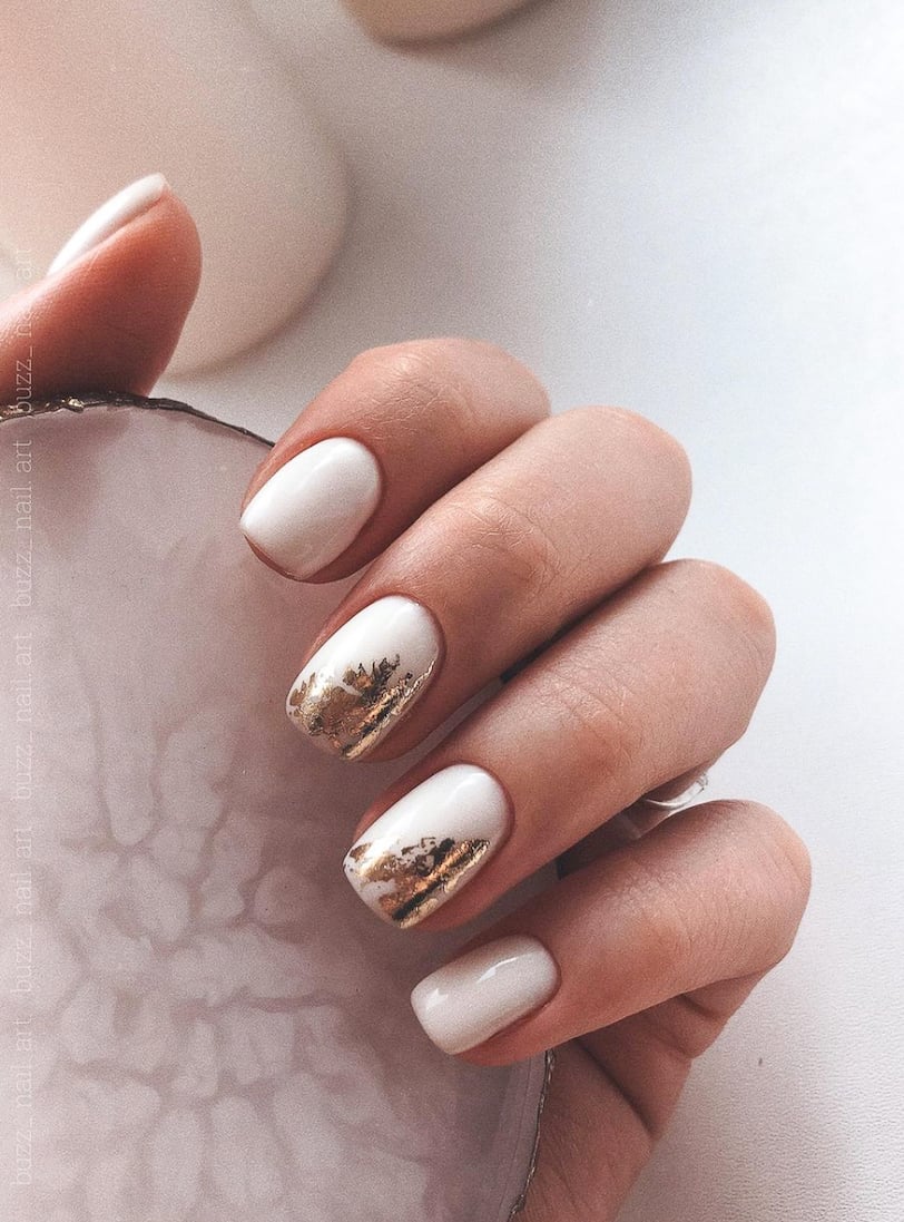 image of a hand with white nails that have gold foil accents