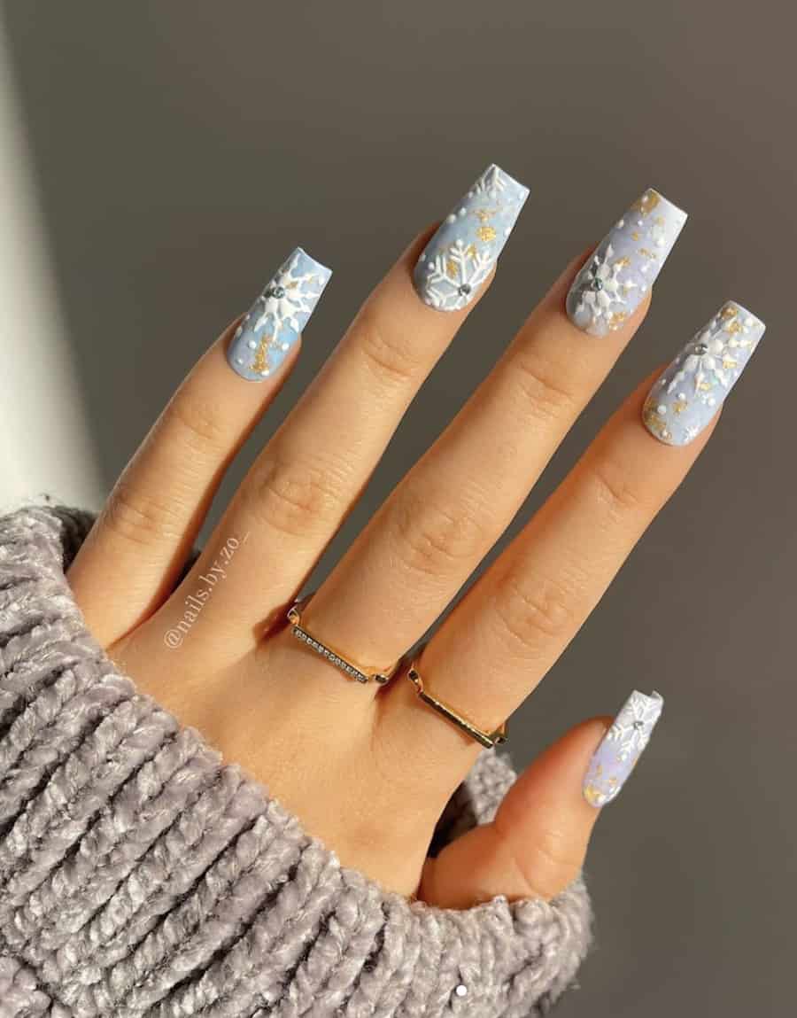 image of a hand with pretty blue nails with snowflakes and gold art