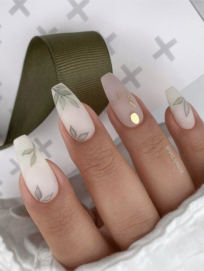 image of a hand with white nails with a eucalyptus leaf design and gold accent