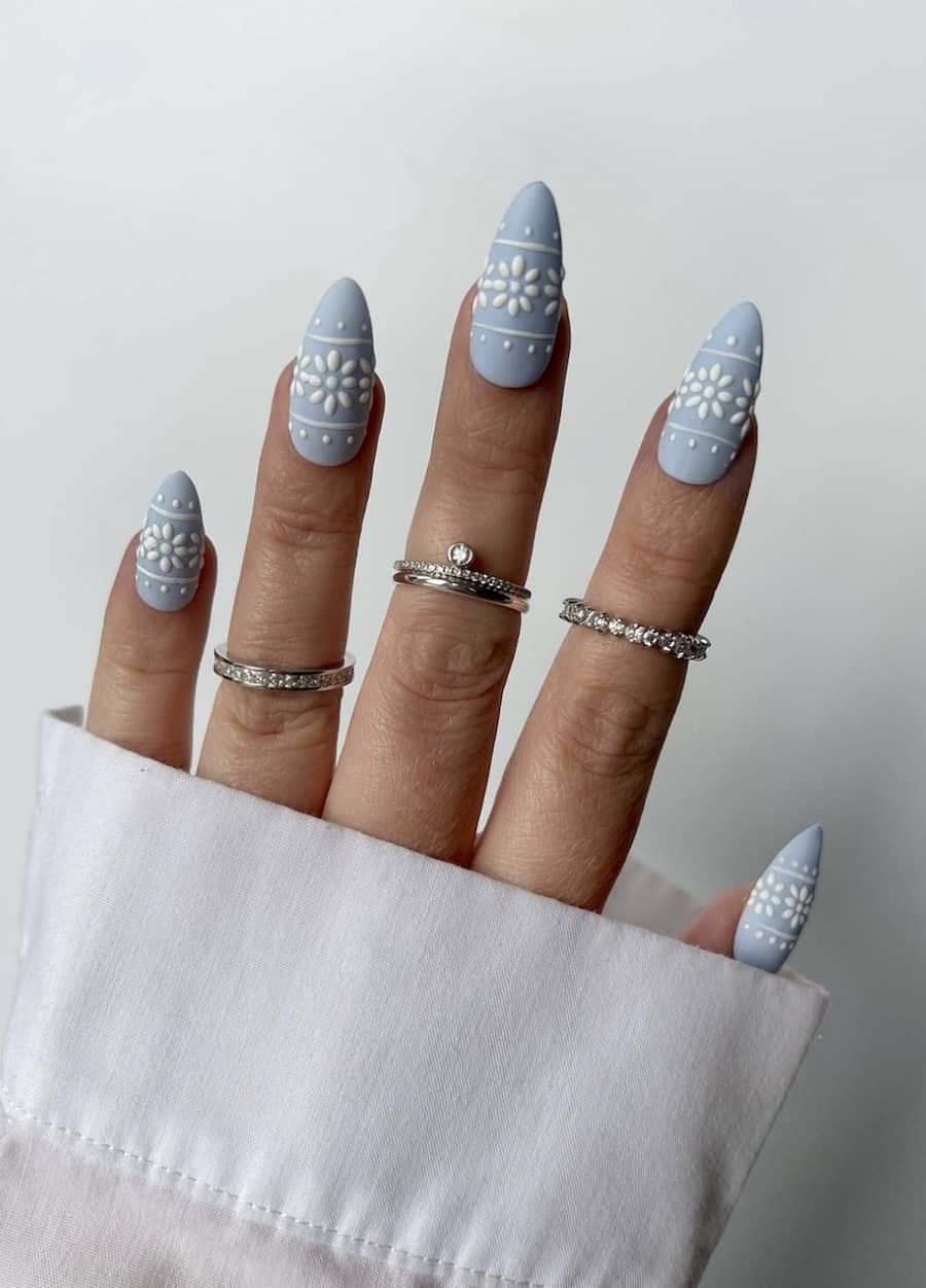 image of a hand with pastel blue nails with a white Christmas pattern