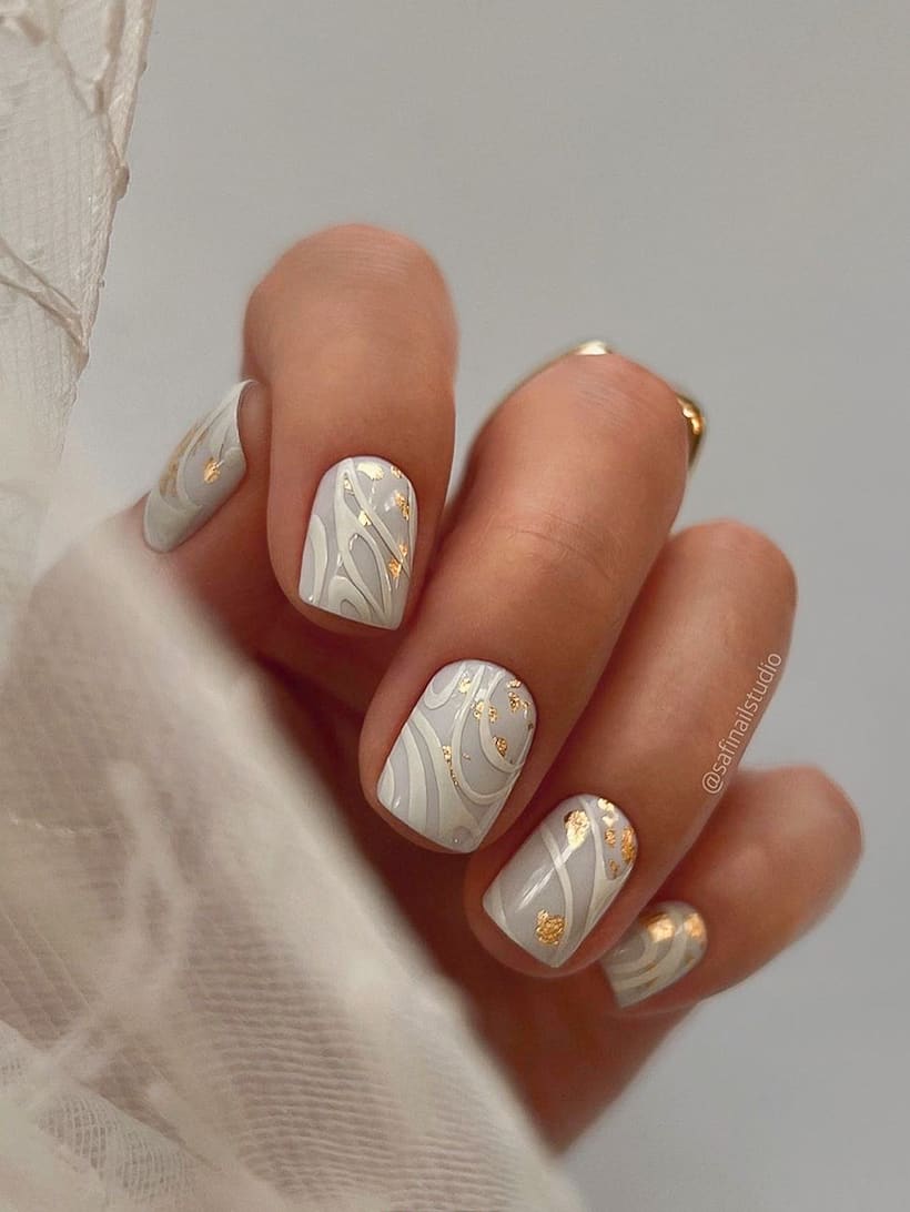 image of a hand with white nails with a swirl gold design