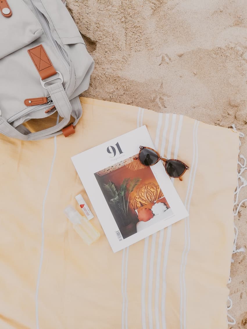 image of a beach towel with a magazine and sunglasses and beach bag