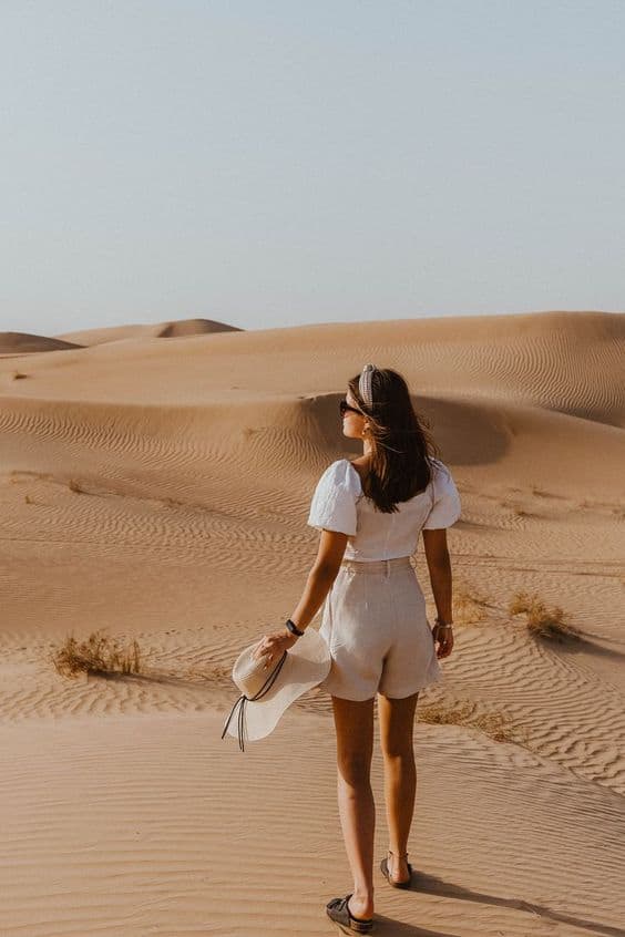 woman in the desert weaning a white blouse and linen shorts
