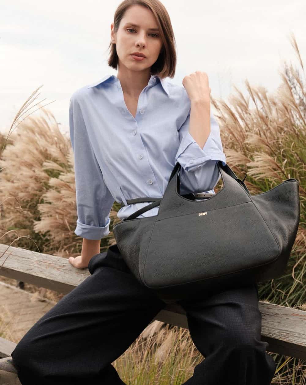 woman wearing a light blue button-up shirt with a large black leather tote