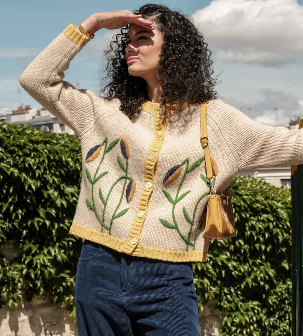 woman wearing an ivory embroidered cardigan with a yellow shoulder bag and blue corduroy pants