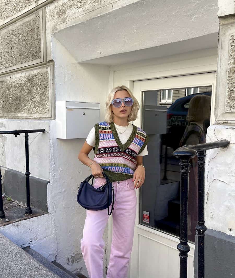 woman wearing a bright knit striped sweater vest and pink jeans with a black handbag