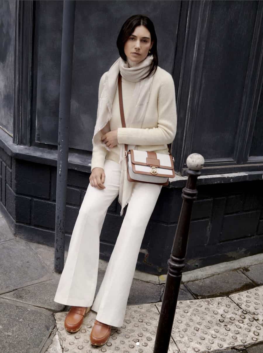woman wearing a cream sweater, ivory pants, and brown shoes with a Longchamp canvas and brown leather crossbody bag