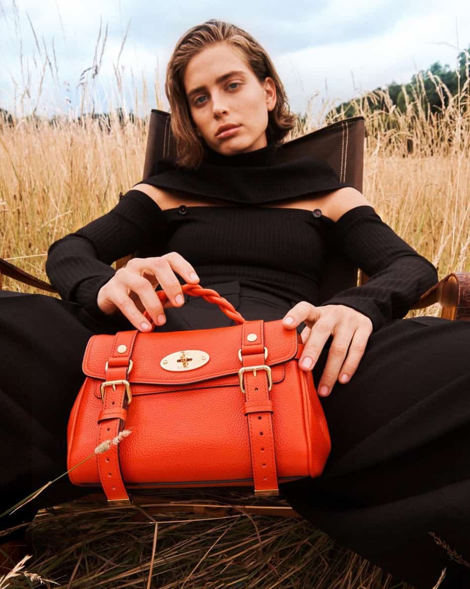 woman leaning back in a chair wearing all black holding a red Mulberry bag