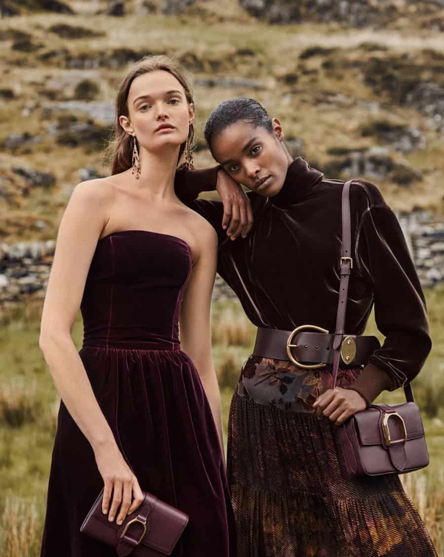 two women wearing dark maroon dresses with maroon leather bags