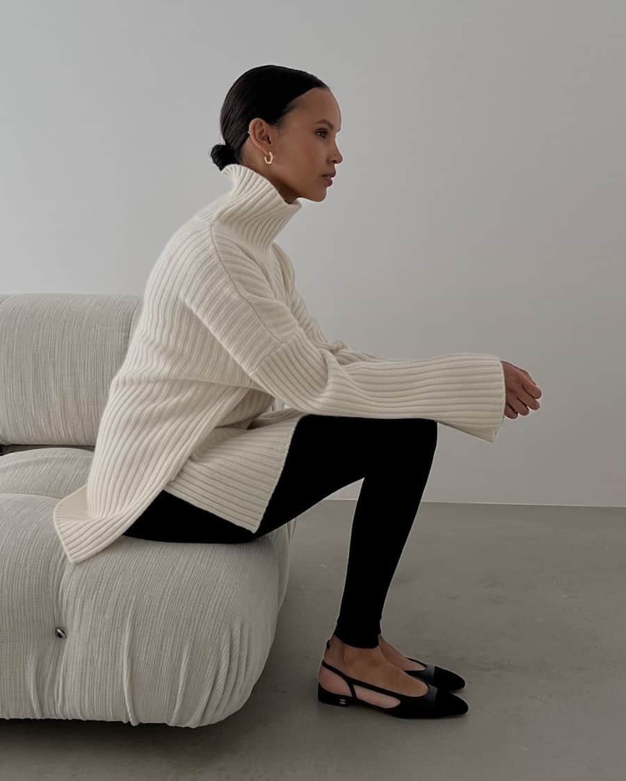 black woman wearing an oversized ivory cashmere turtleneck sweater with black leggings with a stirrup detail and chanel slingback low pumps